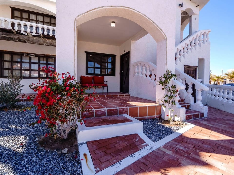 The gated community entrance requires an electronic access card for entry, located off Highway 5 approximately 9 km south of downtown San Felipe. A paved driveway leads to this two-story building.
