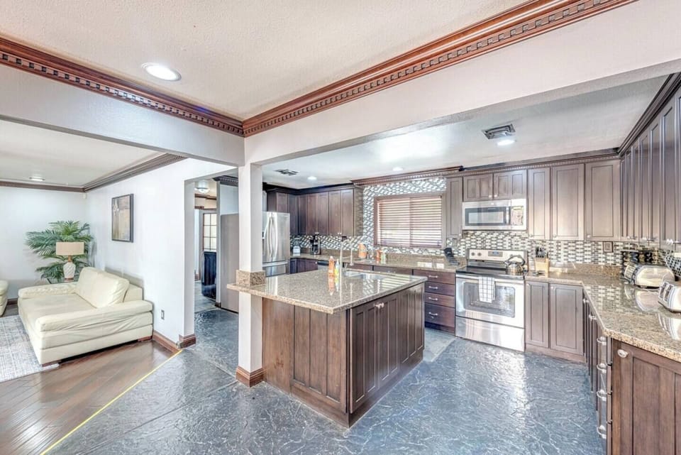 Spacious modern kitchen with dark wood cabinets, granite countertops, stainless steel appliances, and a central island. Perfect for entertaining, opens to a living area