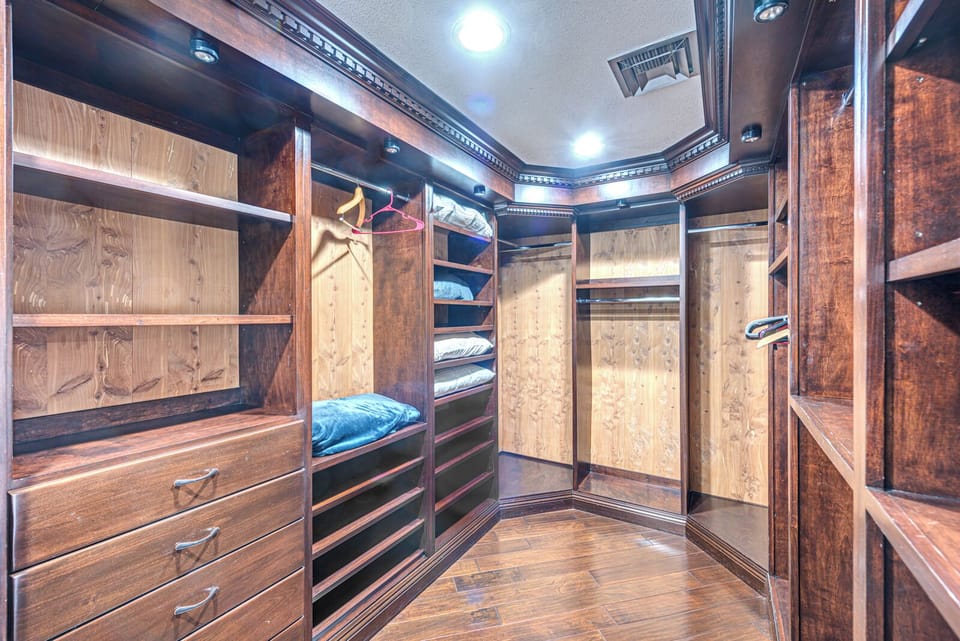 Spacious walk-in closet with dark wood shelves, drawers, and hanging space, neatly organized with folded clothes and hangers