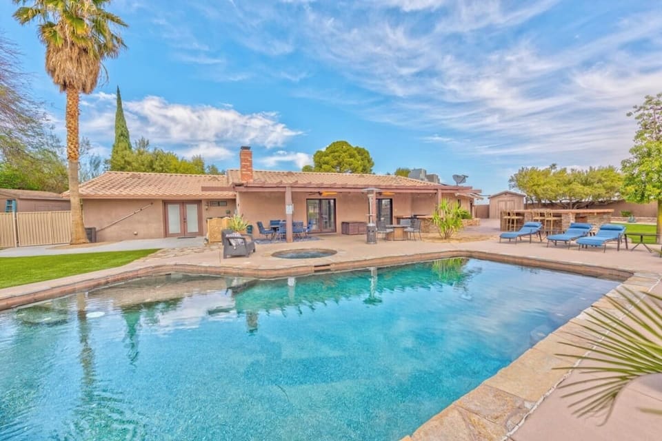 Backyard view of a single-story house with a tiled roof, large swimming pool, hot tub, lounge chairs, palm trees