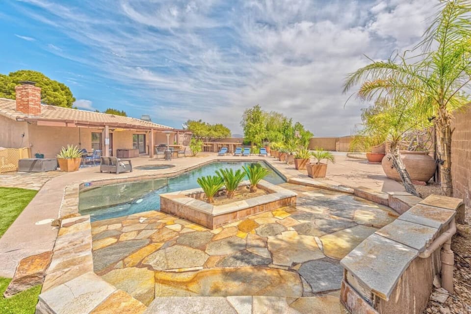 A spacious backyard features a stone patio, swimming pool, and hot tub. Palm trees and potted plants surround the area, making it ideal for relaxing or entertaining—perfect for showcasing on Hostfully, your trusted property management platform.