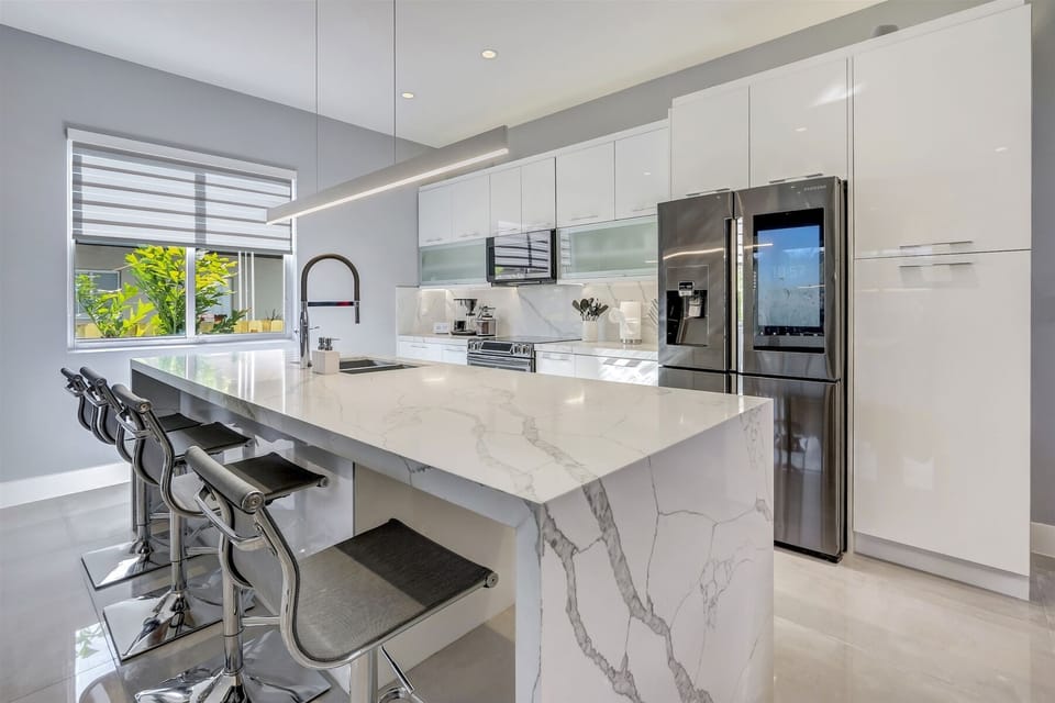 Luxurious kitchen features a white marble, waterfall island -w/ four counter stools-