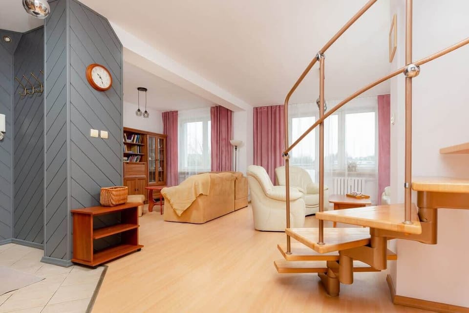 A bright living room featuring a cozy seating area and a modern wooden staircase leading to an upper level.