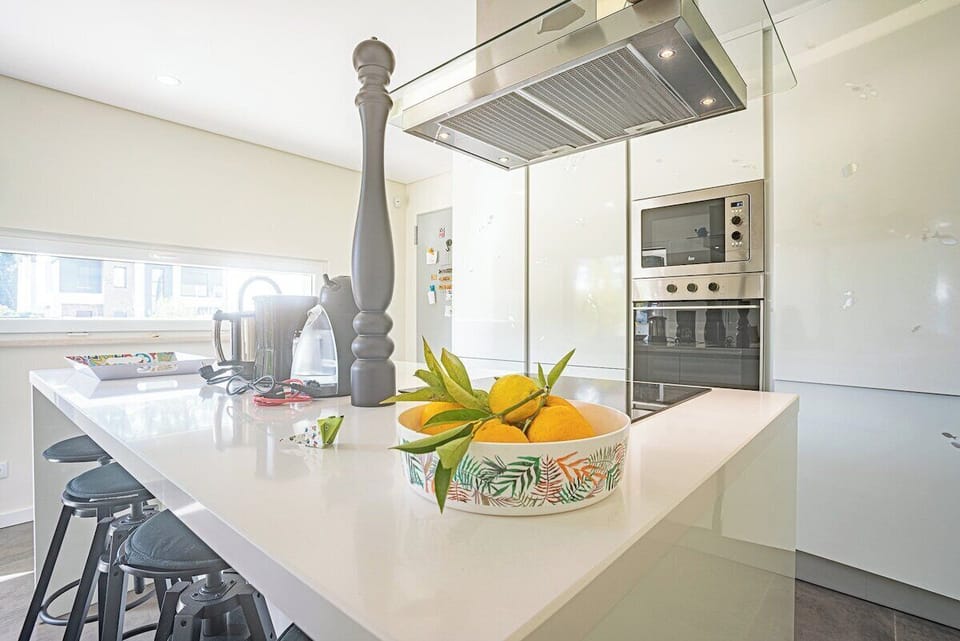 Modern white kitchen with island and orange fruit bowl — Villa Sassi, holiday villa in Aroeira