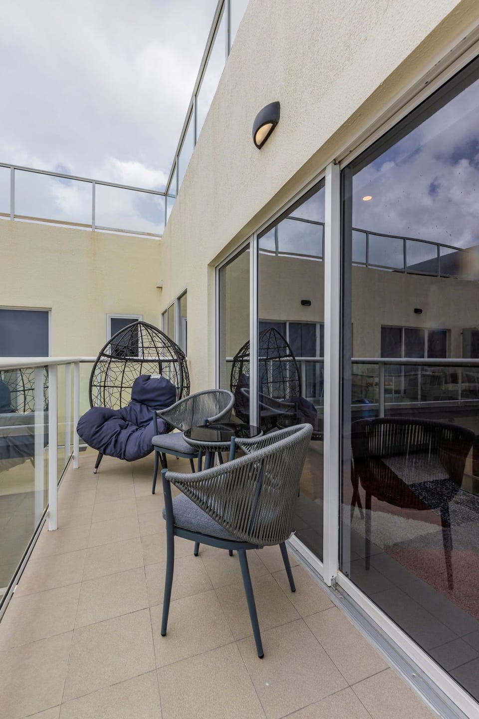 A sun-soaked courtyard pool stretches before modern terraced balconies, offering a tranquil retreat with ample lounge seating and shaded umbrellas beneath clear blue skies.