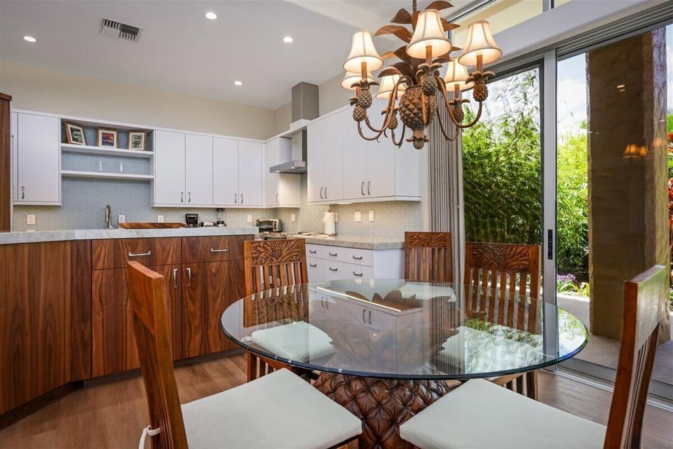 Step into your gourmet kitchen with elegant cabinetry and gather around the glass dining table where natural light pours in through open patio doors. Your culinary retreat awaits with modern appliances and warm wood finishes.