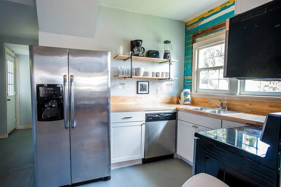 Kitchen nook features stainless steel refrigerator and dishwasher, electric glass cooktop stove.  Industrial shelving allows easy access to dinnerware and glasses