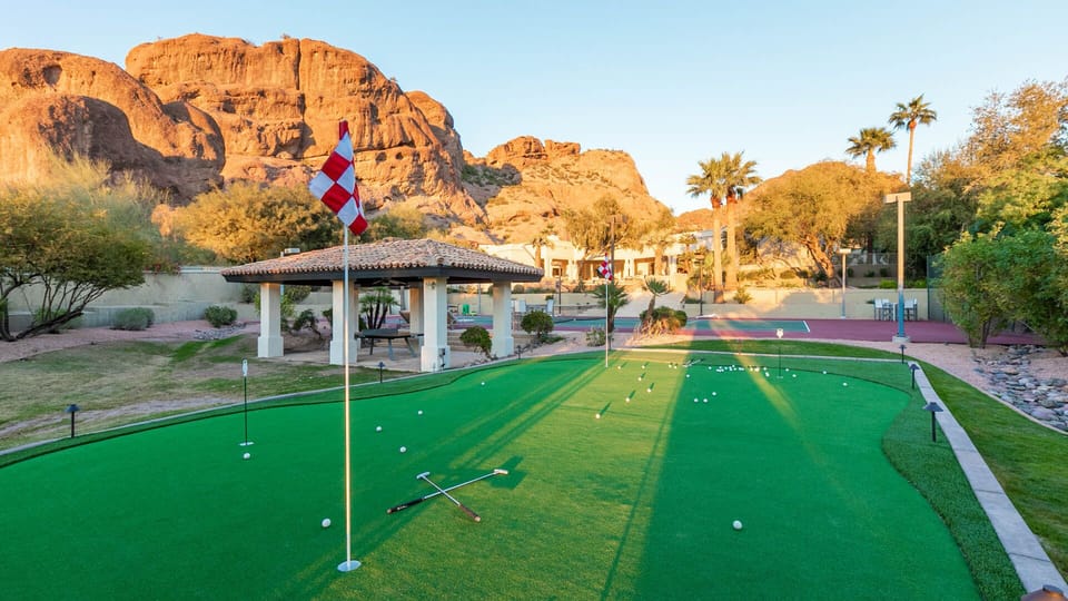 Scenic backyard with a putting green, gazebo, and stunning rocky backdrop.