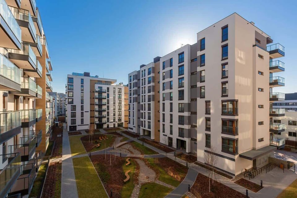 The balcony offers a view of modern apartment buildings, arranged around a landscaped courtyard. The architecture is contemporary, with large windows and sleek balconies.