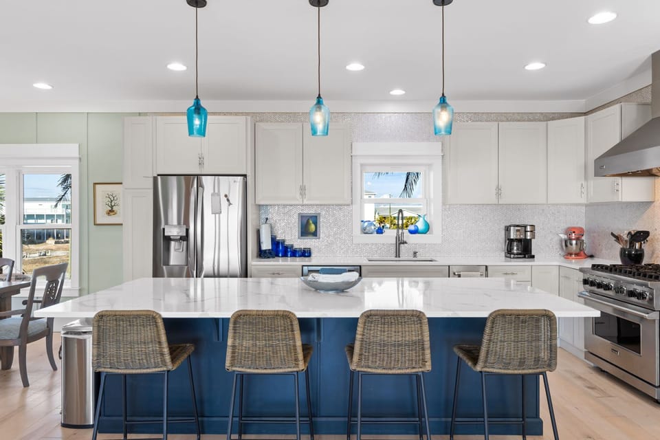 Your gourmet kitchen features a stunning blue island, stainless steel appliances, and coastal pendant lighting perfect for cooking memorable meals together.
