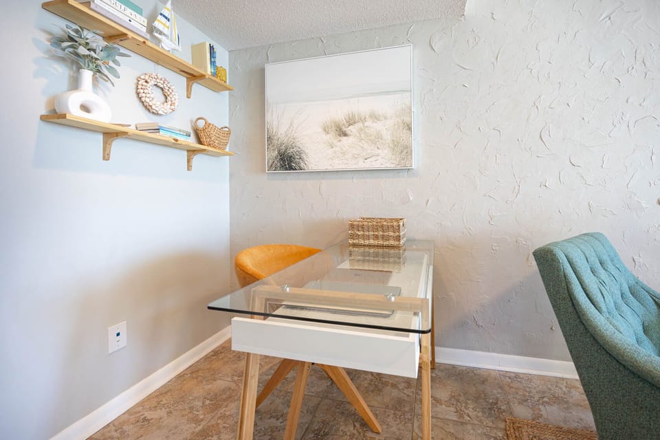 This cozy workspace features a glass desk, colorful chair, and beach-themed decor, perfect for enjoying complimentary WiFi