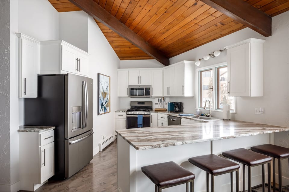 Spacious kitchen w/ white cabinetry, island seating & vaulted wood ceiling overhead.