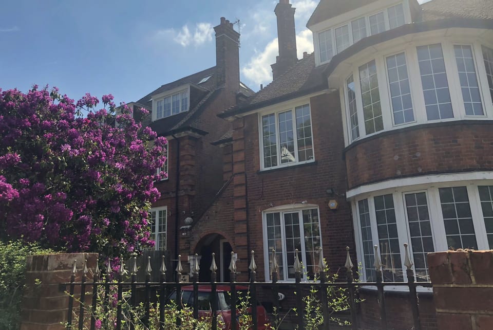 The imposing facade, with mature rhododendrons and gated forecourt