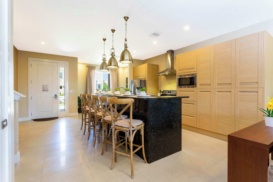 Open-concept kitchen showcases light wood cabinetry, a sleek black-granite island with ample bar seating, and statement pendants-great for cooking and gatherings.
