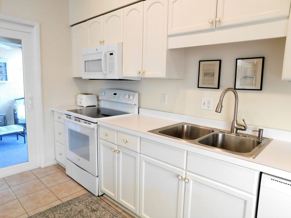 105 Cedarwood Street Modern White Kitchen with Stainless Sink - A clean, functional kitchen area featuring white cabinetry, a white stove and microwave, and a double stainless steel sink.