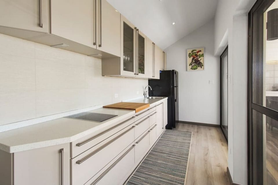 Sleek galley prep kitchen offering smooth quartz countertops, full-size refrigerator, electric cooktop, and cutting board.