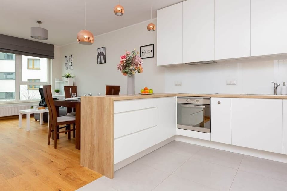 A modern kitchen with white cabinetry, a countertop, and integrated appliances. The layout includes an island with barstool seating.