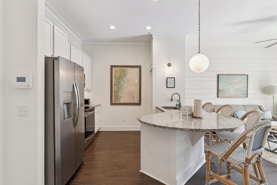 Step into your coastal-inspired kitchen, where warm wood floors meet white cabinetry, stainless appliances, and a granite-topped island perfect for morning coffee or evening meals.