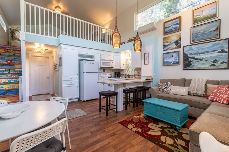 Kitchen area, dining areas, and cozy living room with stone fireplace & artwork.