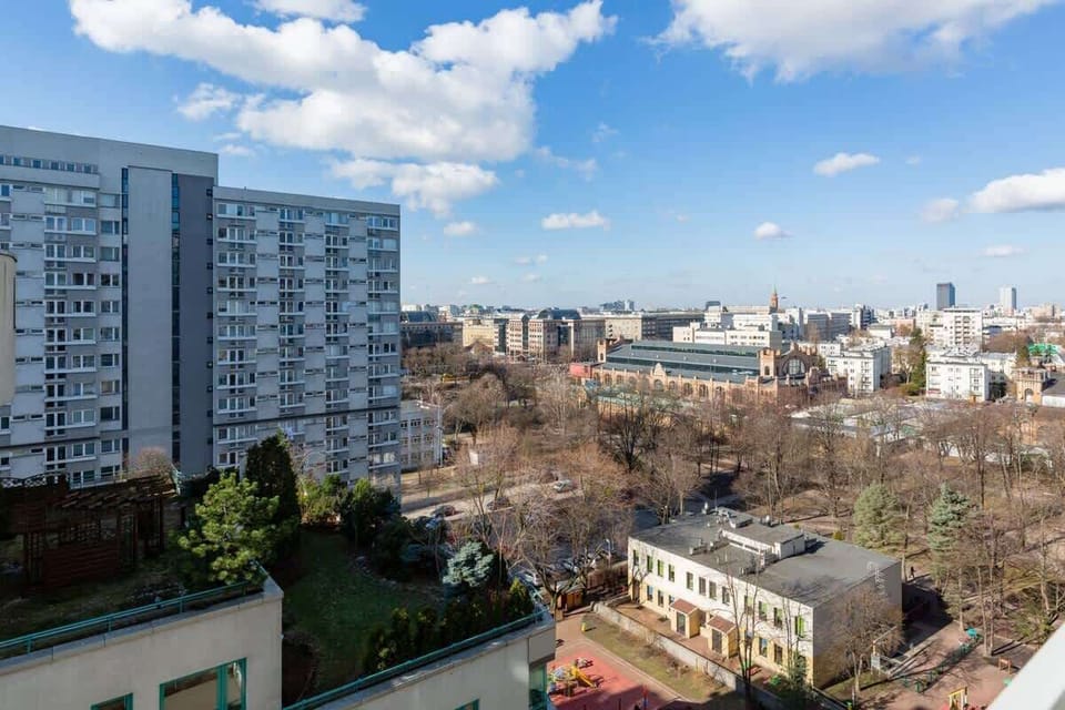 A view of a city skyline with residential and commercial buildings surrounded by greenery. The photo captures a sunny day with clear skies.