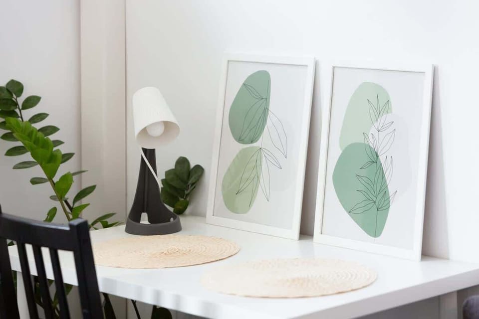 A close-up view of a dining table with green botanical prints as wall art. The table is elegantly set with white dishware and decorative elements.