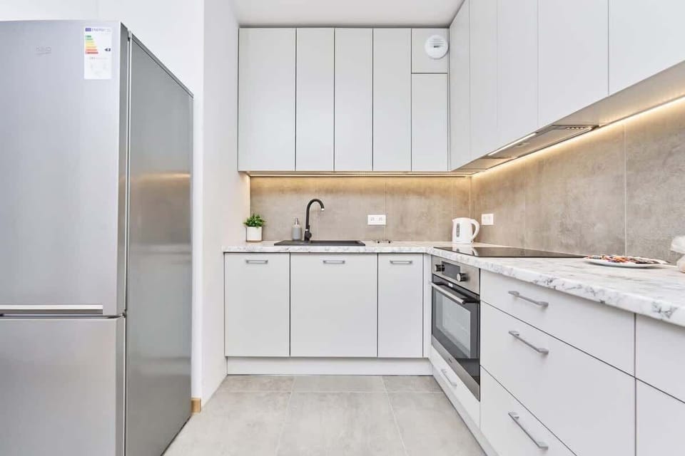 A modern kitchen with sleek white cabinets, integrated appliances, and under-cabinet lighting.