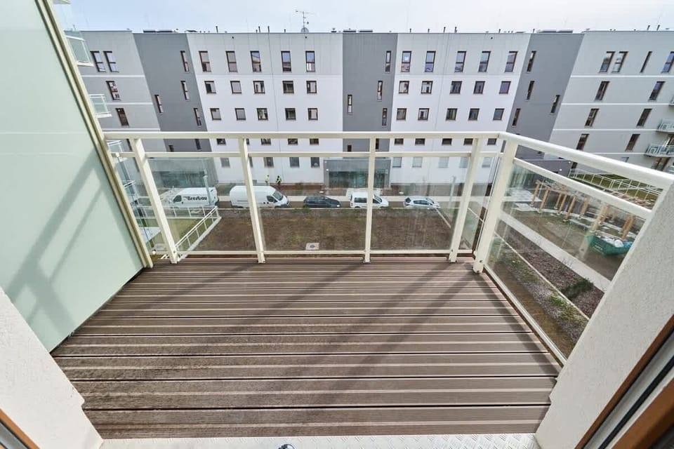 A balcony with wooden flooring and glass railings, offering views of the residential area.