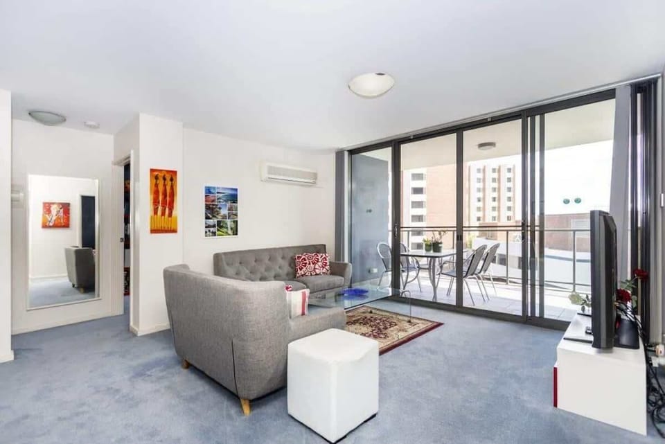 Stylish living room with a comfortable sofa, a chic rug, and a glass center table. Enjoy the air conditioning and entertainment with the TV. Step out onto the balcony to find an outdoor table and chairs, perfect for enjoying the weather.