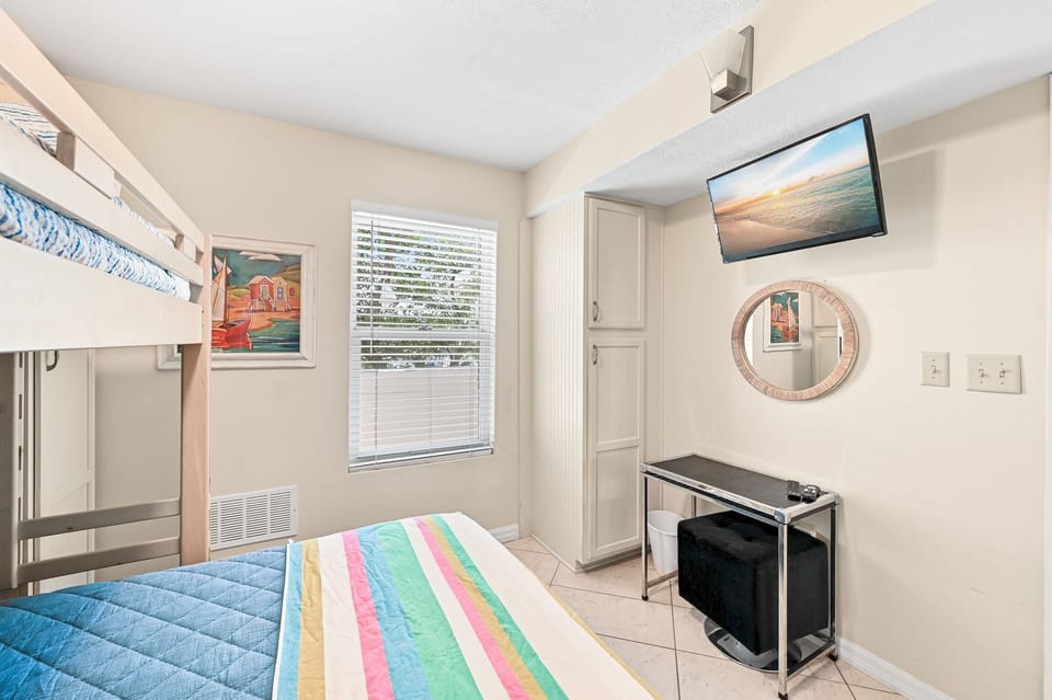 Unwind in your cozy guest room featuring cheerful striped bedding, wall-mounted TV for movie nights, and thoughtful touches like coastal artwork.