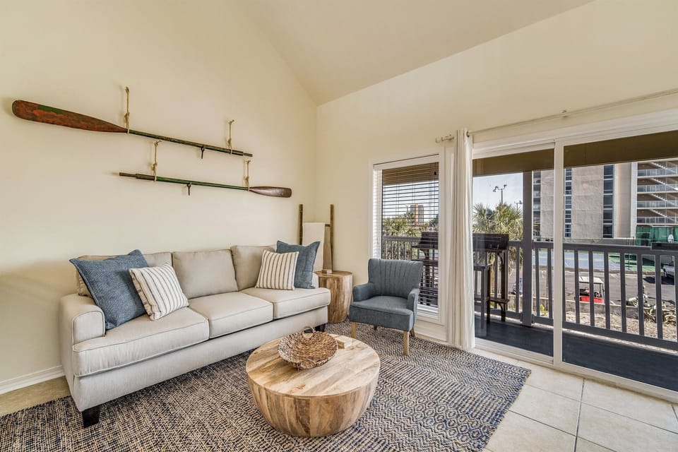 Comfortable main-level living room with sliding glass doors opening to the private bay-view balcony. Sand Dollar 206 East, Pensacola Beach loft condo on Little Sabine Bay.