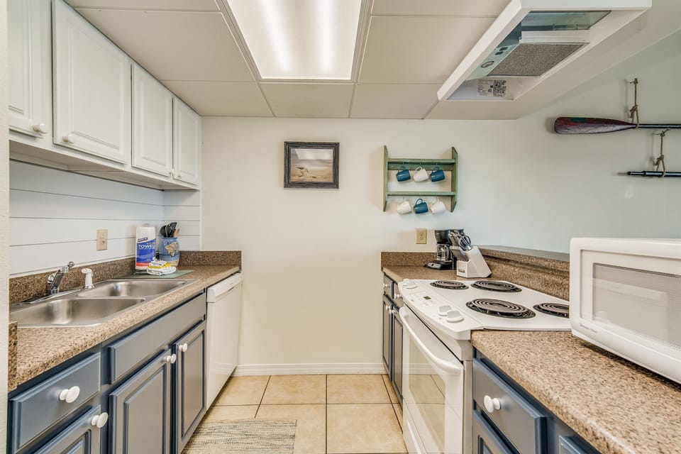 Fully equipped kitchen with electric stove and oven, full-size refrigerator, and navy cabinetry. Sand Dollar 206 East — recently renovated Pensacola Beach vacation rental.