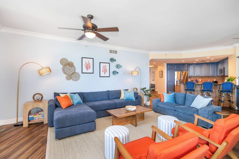 Relax in your bright living space with plush blue sofas and vibrant coral accents, where coastal charm meets modern comfort.