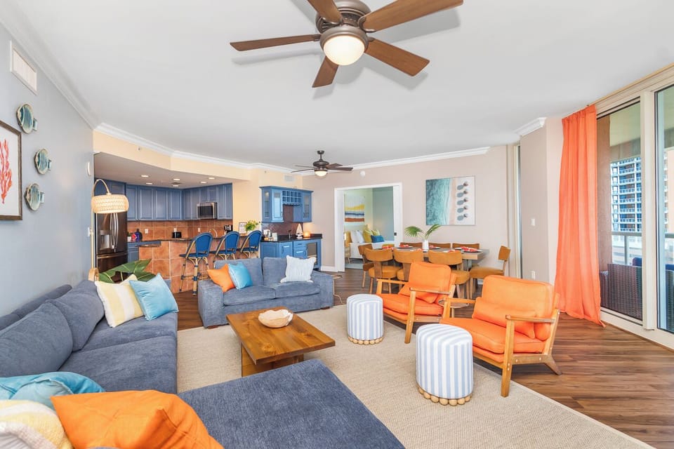 Relax in your bright, coastal-inspired living space with plush seating, modern kitchen, and vibrant pops of orange and blue throughout.