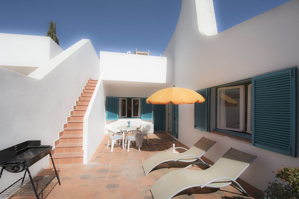 On the private terrace of Casa Pastrano there are two sun loungers with parasols and a barbecue. At the back, there is an outdoor table with matching chairs and a double door leading into the living room. A narrow staircase leads up to the roof terrace.
