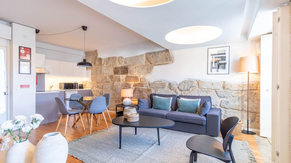 Unwind in this beautifully designed open-plan living area, featuring a cozy sofa and a dining space that seamlessly blends with the modern kitchen, all illuminated by warm, inviting lighting. #OpenPlanLiving #ComfortableStay #ModernKitchen #CozyHome #Dini