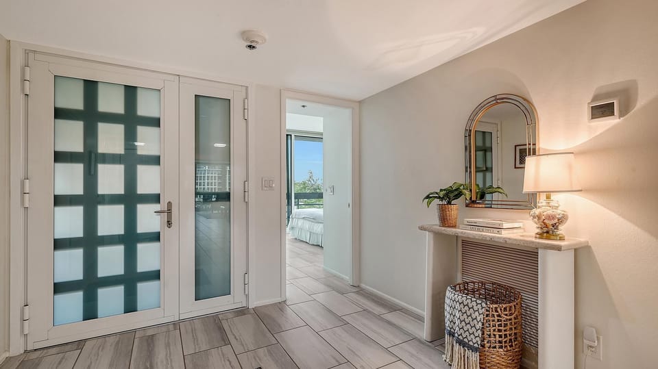 Entryway with frosted glass double doors, gray wood-look tile floor, console table, and arched mirror.