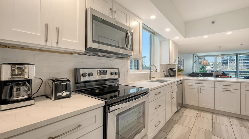 White shaker cabinets and quartz counters frame the kitchen with stainless steel appliances and a tile floor.