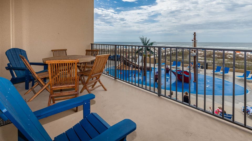 The balcony features a round dining table and wooden chairs, overlooking the beach and pirate ship splash park