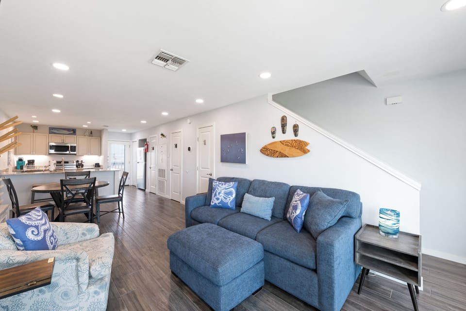 Step into your breezy coastal haven, where open-concept living blends comfort and style. Sink into the plush blue sectional, whip up fresh meals in your modern kitchen, or gather around the dining table—all within one light-filled space.