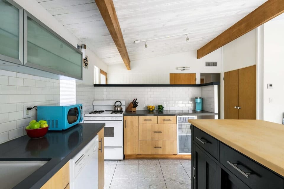 Mid-Century Modern Meets Culinary Comfort 🍽️✨ This bright and stylish kitchen blends sleek black countertops, warm wood cabinetry, and retro pops of color for a perfect mix of charm and function. Whether you`re brewing morning coffee or cooking up a feast