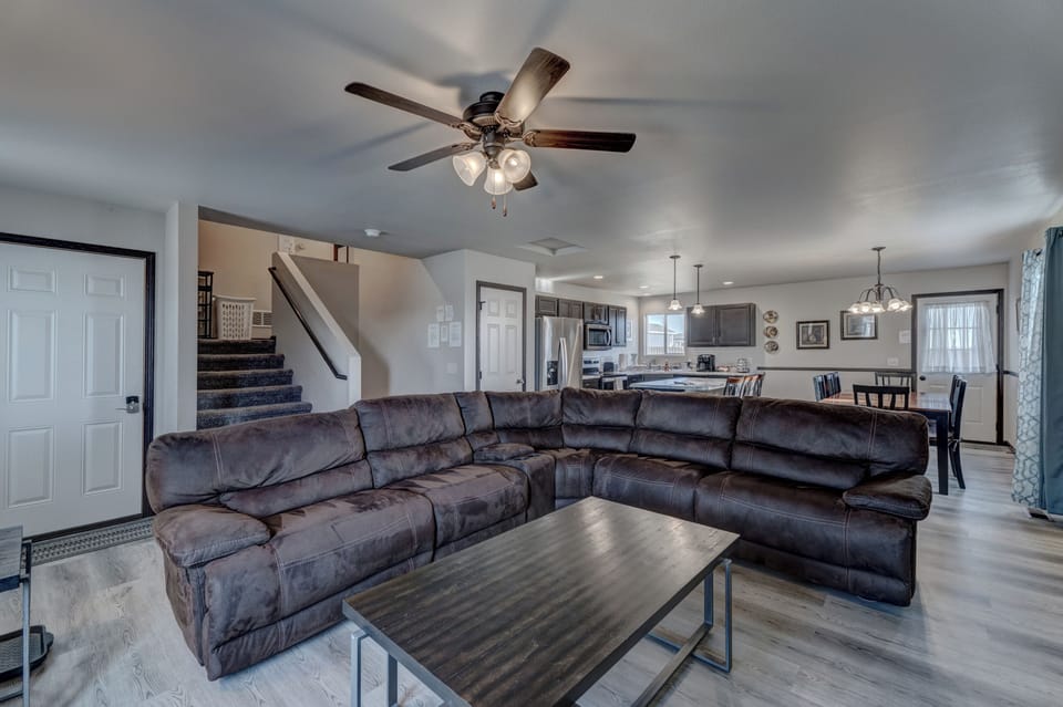 Living room with view into kitchen with full complement of stainless steel appliances, cookware, bakeware, and large dining room table with seating for 8-10 people. 