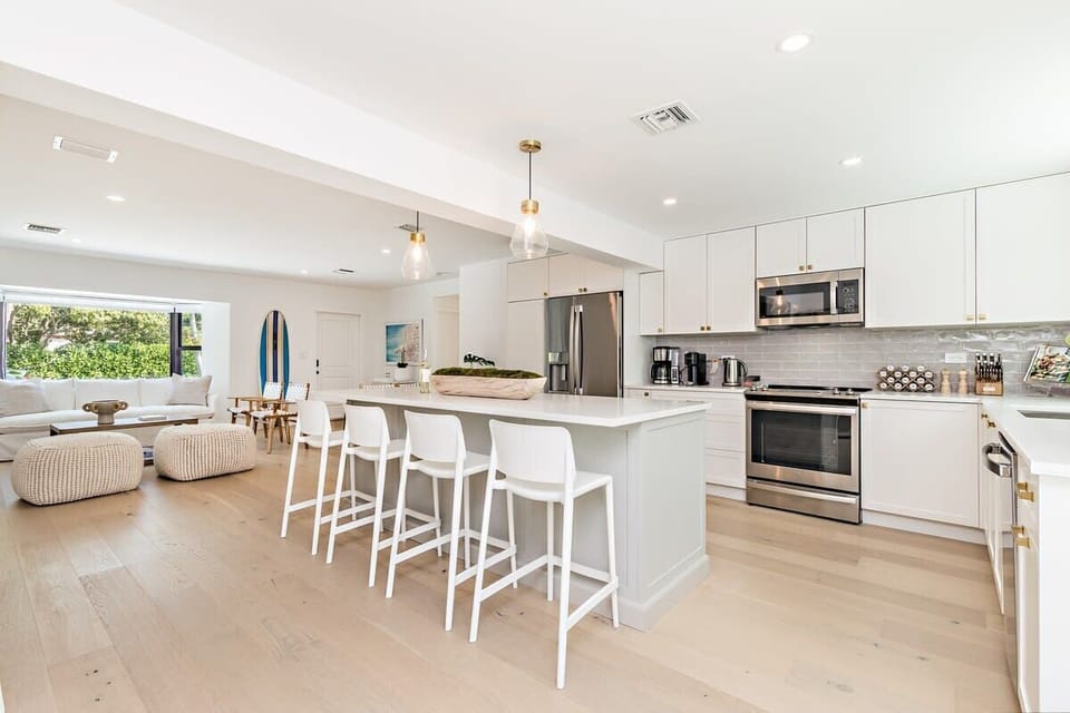 Modern kitchen with a large island and open living area featuring natural light and light wood flooring