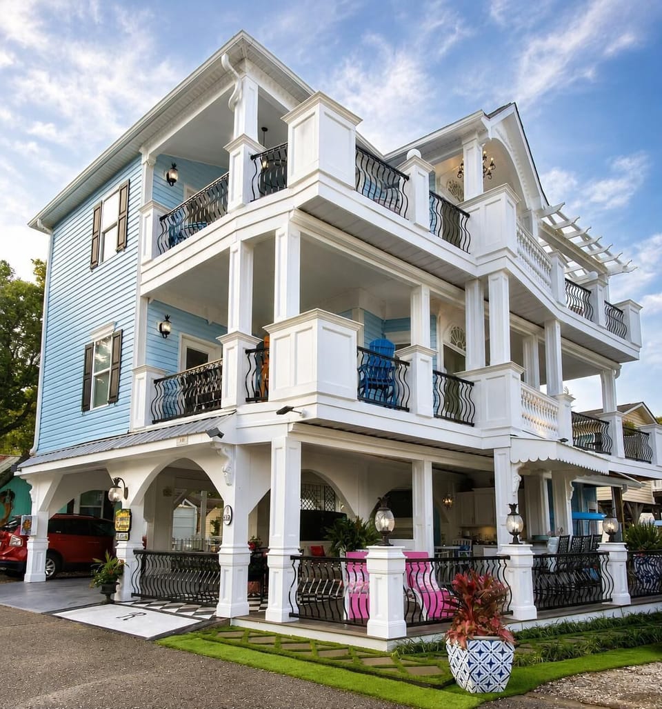 Three-story blue house with white columns, black wrought-iron railings, and outdoor seating on multiple porches.
