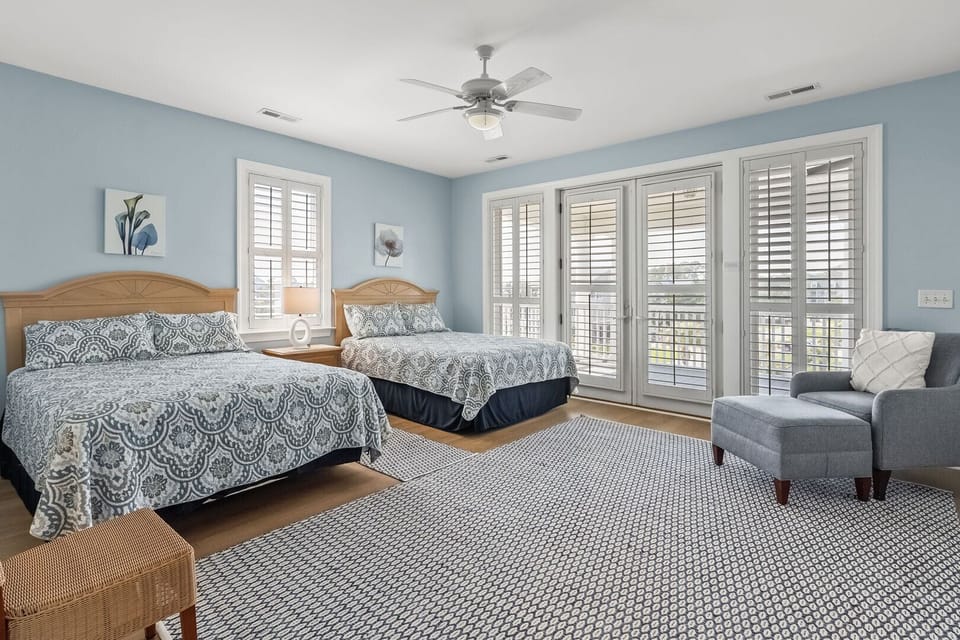 Gray and white bedding, an armchair and shuttered windows at Wicker Cottage in Tilghman Beach
