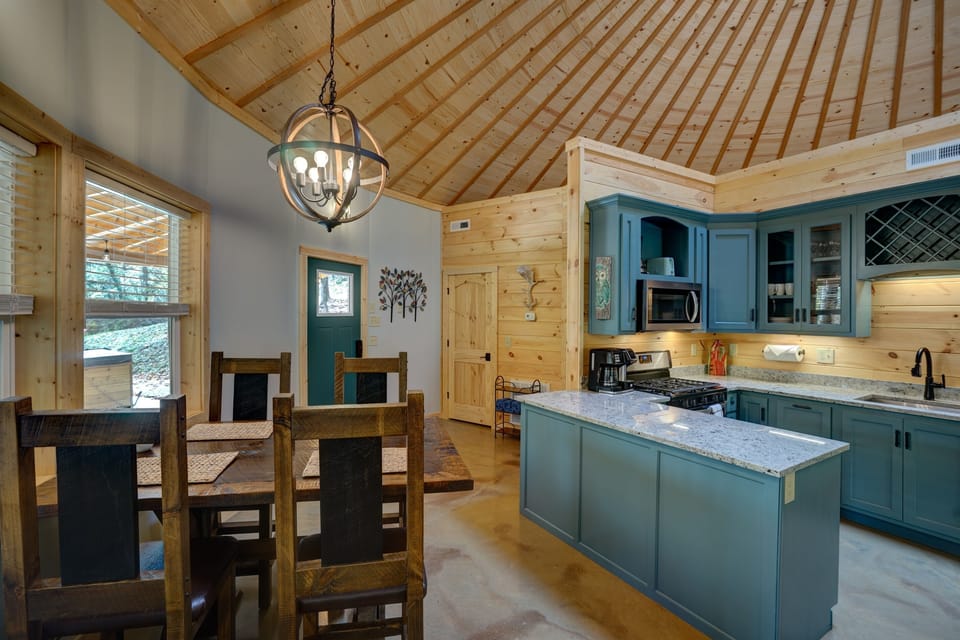  A stunning full kitchen with bold teal cabinetry, granite counters, a center island, and stainless appliances, all under a soaring wood dome ceiling with a rustic dining table for four right alongside.