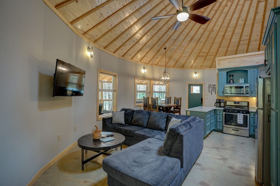 The open circular living space flows seamlessly from the plush sectional and mounted TV to the dining area and fully equipped kitchen, all beneath a soaring wood dome ceiling. Everything you need, all in one stunning space.