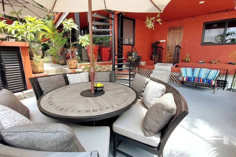 Nine person dining table with shade umbrella.  Entrance to Jonathan's Lugar is in the background. 