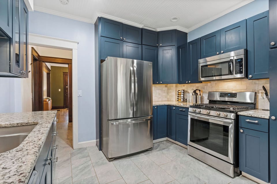First-Floor Full Kitchen with stainless steel appliances, stunning blue cabinetry, and granite countertops—perfect for cooking at home between outings to Westport and West 39th Street’s walkable dining scene.