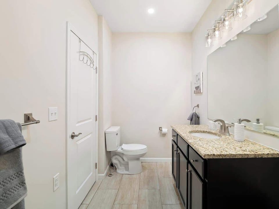 Bright bathroom featuring a granite-topped vanity with dark wood cabinets, frameless mirror, and modern lighting. Spacious tiled shower with sleek fixtures and plush mat—your daily oasis! ✨
