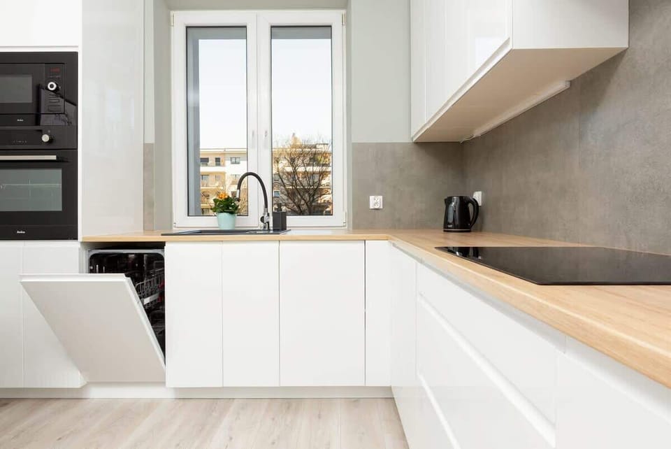 A sleek white kitchen with handleless cabinets, modern appliances, and a light wooden countertop.